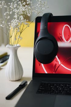 A sleek laptop with black headphones and a vase with flowers create a modern workspace setting.